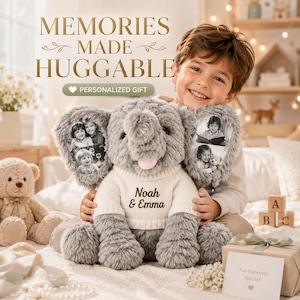 May include: A gray plush elephant toy wearing a cream-colored knit sweater with the text Noah & Emma embroidered on the front. The elephant features two large ears with black and white printed photographs of children on each side.