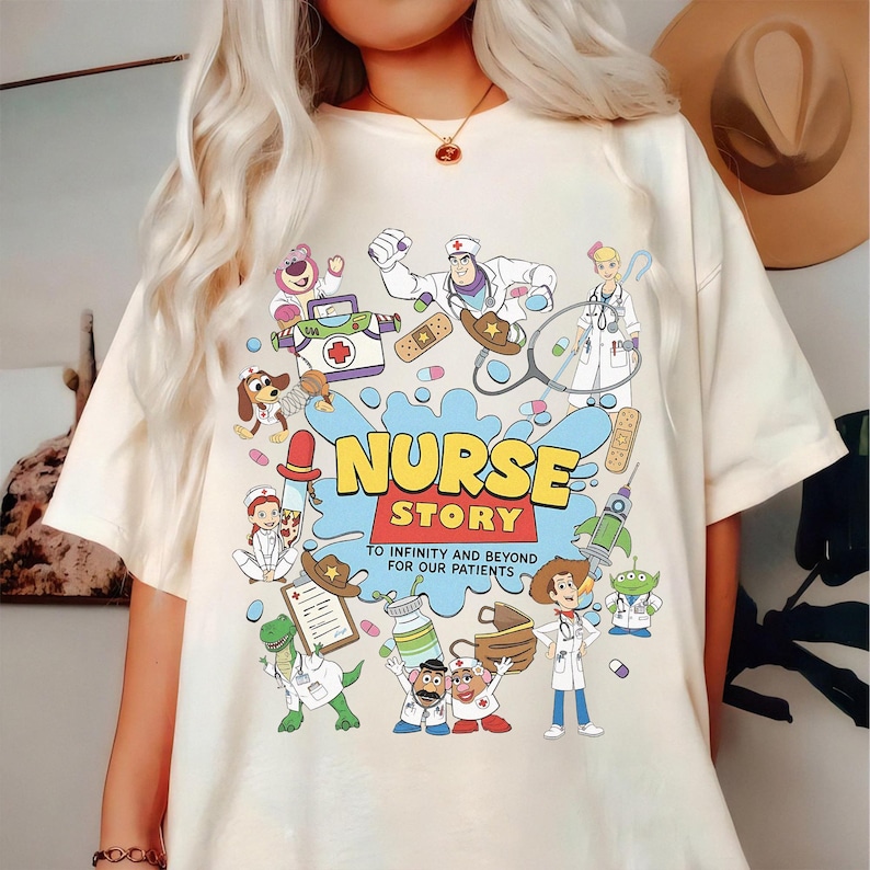 May include: Cream-colored t-shirt with a colorful graphic featuring cartoon characters in medical attire. The design includes the words "NURSE STORY" and "TO INFINITY AND BEYOND FOR OUR PATIENTS". The shirt has a crew neck and short sleeves.
