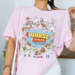 May include: Pink t-shirt with a colorful graphic featuring cartoon characters and the text "NURSE STORY" in yellow and blue. The design includes medical equipment and the phrase "TO INFINITY AND BEYOND FOR OUR PATIENTS".