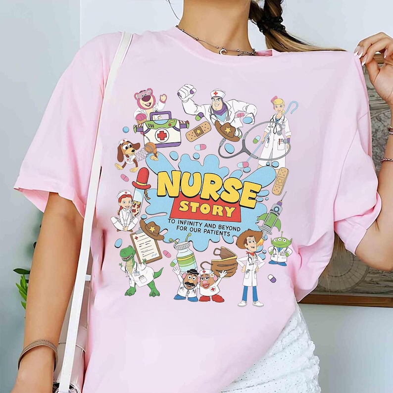 May include: Pink t-shirt with a colorful graphic featuring cartoon characters and the text "NURSE STORY" in yellow and blue. The design includes medical equipment and the phrase "TO INFINITY AND BEYOND FOR OUR PATIENTS".