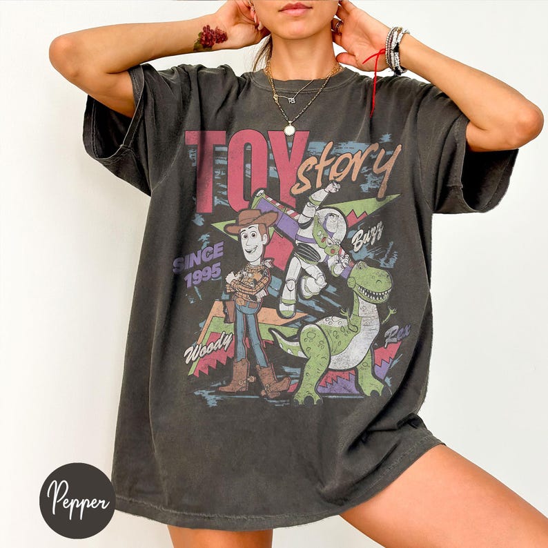 Puede incluir: Camiseta gris oscuro con un gr&aacute;fico de Toy Story. El dise&ntilde;o incluye a Woody, Buzz Lightyear y Rex, con las palabras "Toy Story" y "Since 1995". La camiseta tiene un aspecto vintage y desgastado.