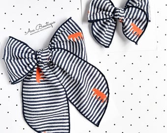 May include: Two hair bows featuring a navy blue and white horizontal striped pattern with small orange tiger silhouettes. Each bow is attached to a white display card labeled Ava Bowtique Handmade Accessories in black script text.