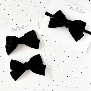 May include: Three black velvet hair bows on white cards with the text "Ava Boutique HANDMADE ACCESSORIES" on a white background with black polka dots. One bow is on a headband.