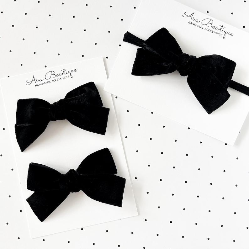 May include: Three black velvet hair bows on white cards with the text "Ava Boutique HANDMADE ACCESSORIES" on a white background with black polka dots. One bow is on a headband.