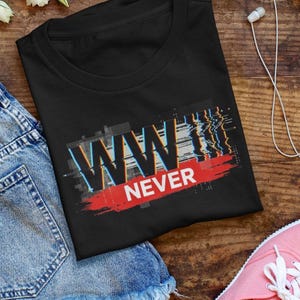 Może przedstawiać: Czarny t-shirt z napisem "WWIII NEVER" w efekcie glitch. Grafika zawiera kolory niebieski, czerwony i biały. Koszulka jest złożona na drewnianej powierzchni.