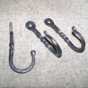 May include: Three hand-forged metal hooks. The hooks are dark gray with a twisted design on the stems. One hook has a straight stem, while the other two have a curved hook shape. The hooks are designed for hanging items.