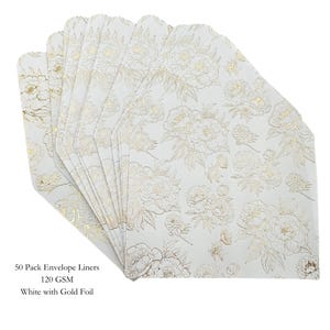May include: A stack of white envelope liners with a gold floral pattern. The liners are made of 120 GSM paper and are white with gold foil accents. The text on the image reads: "50 Pack Envelope Liners 120 GSM White with Gold Foil."
