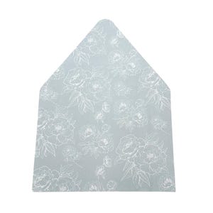 May include: A light blue, house-shaped placemat with a white floral pattern. The design features detailed outlines of peonies and leaves, creating a delicate and elegant aesthetic. The placemat is likely made of a durable, washable material.