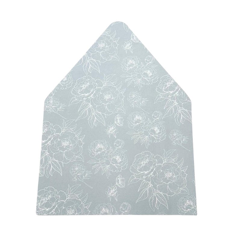 May include: A light blue, house-shaped placemat with a white floral pattern. The design features detailed outlines of peonies and leaves, creating a delicate and elegant aesthetic. The placemat is likely made of a durable, washable material.