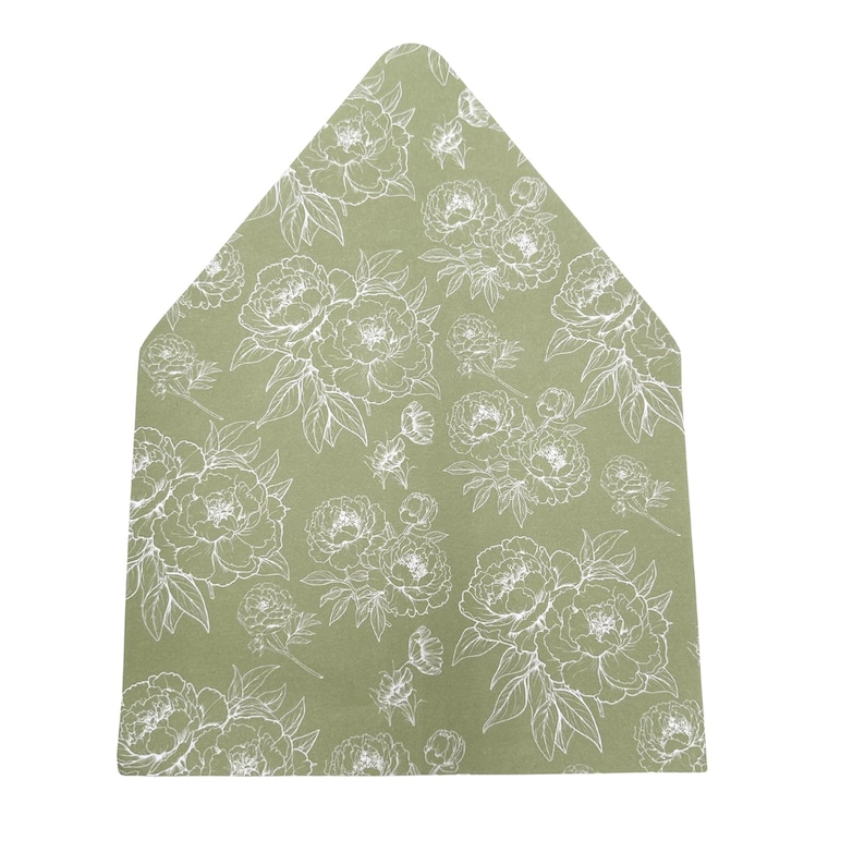 May include: A sage green envelope with a white floral pattern featuring peony blooms and leaves. The envelope has a unique, pointed top and is likely used for invitations or stationery.