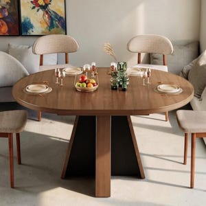 May include: A round wooden dining table with a dark brown finish and a central pedestal base, surrounded by four chairs with light beige upholstered seats and wooden frames. The table is set with white plates, glassware, and a fruit bowl.