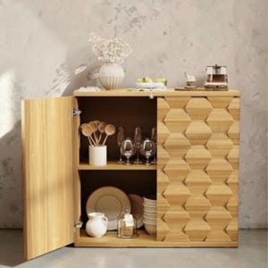May include: A light wood cabinet with an open door, revealing shelves with dishes, glasses, and decorative items. The cabinet's front features a geometric pattern. A vase of flowers and other items sit on top.