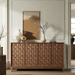 May include: A wooden cabinet with four doors, featuring a woven pattern. The cabinet is a warm brown color and is set against a neutral-toned wall. Decorative vases and a framed landscape painting are on top of the cabinet.