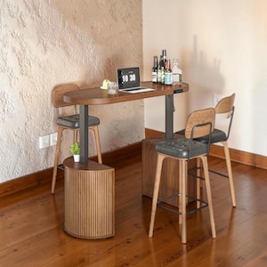 May include: A modern home bar setup with a dark wood table, two bar stools, and a small cabinet. The table has a laptop and bottles on it. The bar stools have black seats and wooden frames. The cabinet is made of wood with vertical grooves.