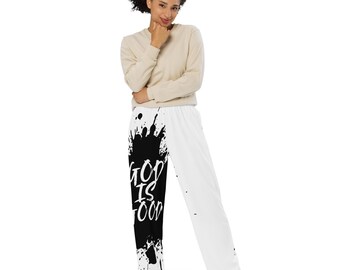 May include: White and black palazzo pants with the text "GOD IS FOOD" in a black splatter design on the left leg. The right leg is solid white. The model is wearing a beige long-sleeve shirt.