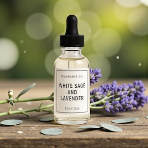 Può includere: Una bottiglia di olio profumato in vetro trasparente con un contagocce nero, etichettata "White Sage and Lavender". La bottiglia è accanto a un rametto di lavanda e foglie verdi. L'etichetta indica anche 60 ml di olio.