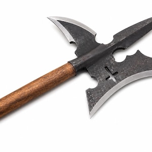 May include: A polearm featuring a dark, textured metal head with a central spike, two curved blades, and a cross-shaped cutout. The metal head is securely attached to a long, straight, brown wooden shaft with a visible grain pattern.