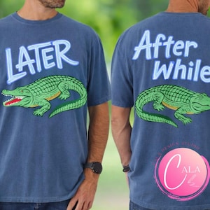 Peut inclure: T-shirt bleu à manches courtes avec un motif d'alligator vert et le mot "LATER" sur le devant. Le dos du t-shirt porte les mots "After While" et un motif d'alligator assorti.