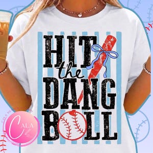 May include: White t-shirt with the text "HIT the DANG BALL" in black block letters. A red baseball bat with a blue bow is featured on the right. A baseball is at the bottom. Light blue vertical stripes are behind the text.