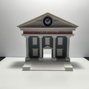 Può includere: Un modello in miniatura di un edificio con facciata bianca, colonne e frontone. Le parole "DEPARTMENT OF SOCIAL SERVICES" sono in rosso. Un orologio è visibile sul frontone. L'edificio ha un esterno grigio e una scala bianca.