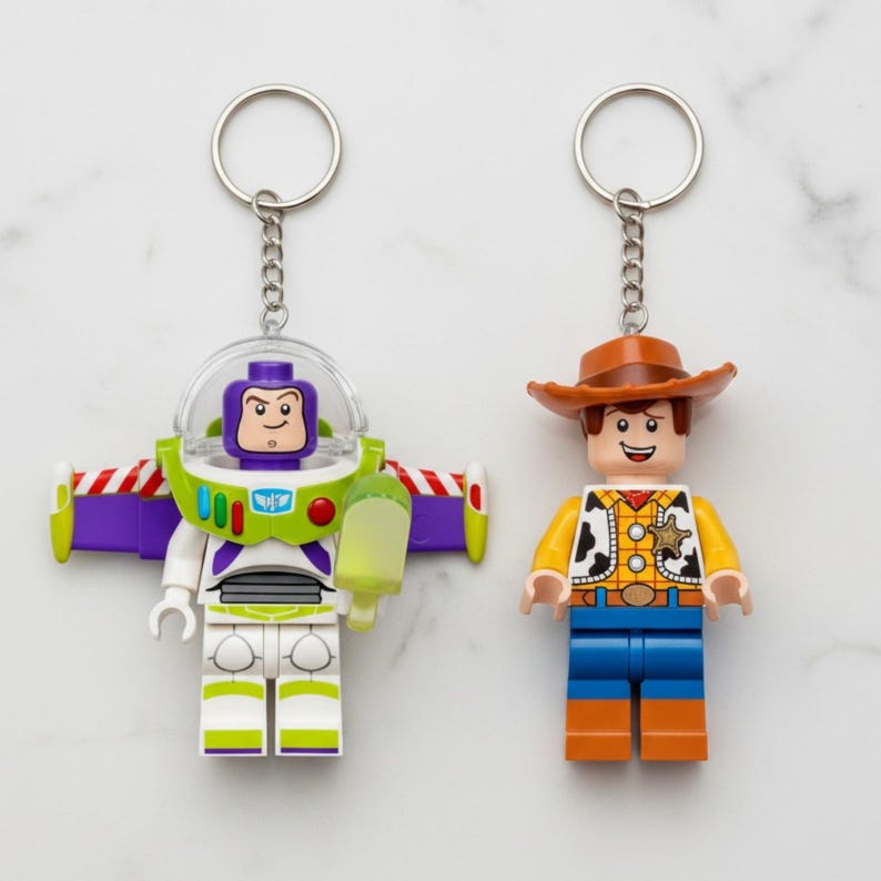 Peut inclure: Deux porte-cl&eacute;s avec des figurines de style Lego. L'un est Buzz l'&Eacute;clair dans une combinaison spatiale blanche, verte et violette avec un casque transparent. L'autre est Woody, un cow-boy avec un chapeau marron, une chemise jaune et un pantalon bleu. Les deux ont des porte-cl&eacute;s argent&eacute;s.