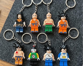 Puede incluir: Una colección de ocho llaveros de personajes con minifiguras de plástico con diversos atuendos y peinados. Cada figura está unida a una anilla de metal plateado mediante una cadena corta, mostrando expresiones pintadas detalladas y ropa colorida.