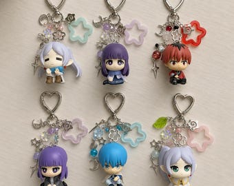 Puede incluir: Seis llaveros con figuras de personajes estilo anime unidas a cierres plateados en forma de corazón. Cada llavero incluye dijes variados como estrellas, lunas y cuentas en diversos colores como azul claro, morado, rojo y blanco.