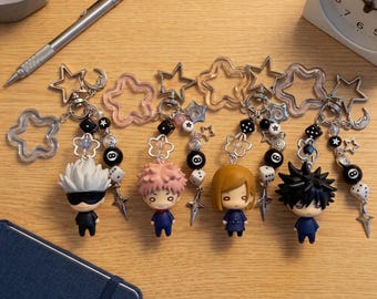 May include: Four anime character keychains featuring chibi figures with white, pink, brown, and black hair. Each keychain includes a star-shaped clasp, black and white beads, dice, eight-ball charms, and small metal star accents on silver chains.
