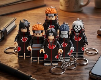 Puede incluir: Una colección de seis llaveros de personajes con figuras estilizadas que visten capas negras con patrones de nubes rojas. Cada figura tiene un peinado y expresión facial únicos, unidos a una cadena de metal plateado y una anilla circular.