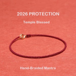 May include: A hand-braided burgundy bracelet with a gold clasp. The bracelet is displayed on a red background. Text on the image reads "2026 PROTECTION", "Temple Blessed", and "Hand-Braided Mantra".