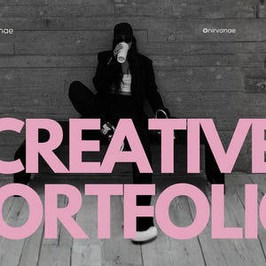 May include: A person in a black outfit and cap is seated, holding a cup, with the words "CREATIVE PORTFOLIO" in pink block letters in the foreground. The background features a gray brick wall and wooden floor.