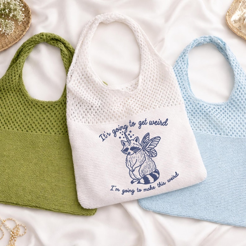Puede incluir: Tres bolsos de mano de punto en verde, blanco y azul. El bolso blanco presenta una ilustraci&oacute;n de mapache con el texto "It's going to get weird. I'm going to make this weird."