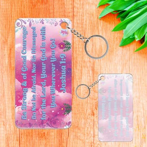 May include: Two rectangular keychains with silver key rings. The keychains have a pink and purple watercolor background with the text "Be Strong & of Good Courage, Do Not Be Afraid, Nor Be Dismayed for the Lord, Your God is with You Wherever You Go! Joshua 1:9."