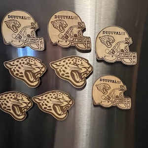 May include: Wooden magnets featuring a football helmet design with the text "DUUUVAL!!!" and a jaguar logo. Also included are magnets with a jaguar head design. The magnets are made of light brown wood.