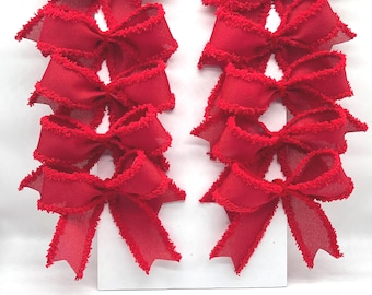 May include: Ten bright red fabric bows arranged in two vertical columns of five. Each bow features a textured, frayed edge along the ribbon loops and tails. The bows are attached to a plain white rectangular backing card for display and storage.