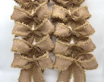 May include: A collection of ten tan burlap bows arranged in two vertical columns of five. Each bow features a coarse, woven texture with frayed, uneven edges and a central knot, creating a rustic appearance across all individual pieces.