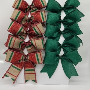 Op de afbeelding: Een set van 10 handgemaakte kerstversieringen, 5 rode en groene gestreepte strikken en 5 effen groene strikken. De strikken zijn gemaakt van jute en glitterstof.