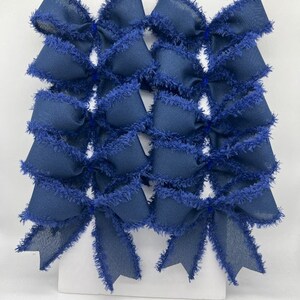 May include: A collection of navy blue fabric bows with frayed edges. The bows are arranged in a grid pattern, showcasing their layered design and textured details. These decorative bows are suitable for various crafting and gift-wrapping projects.