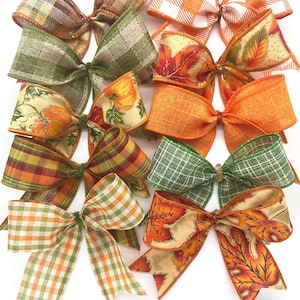 May include: A collection of ten decorative fabric bows featuring various autumn-themed patterns including orange and white buffalo check, green and tan plaid, pumpkin prints, solid orange burlap, and colourful fall leaf motifs on a light background.