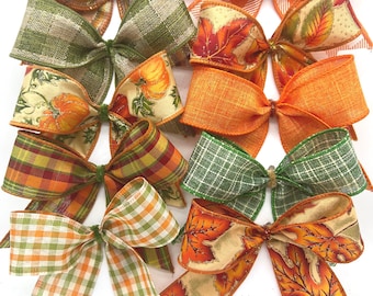 Op de afbeelding: Een verzameling van tien decoratieve stoffen strikken met diverse herfstthema patronen, waaronder oranje en wit ruitpatroon, groen en beige plaid, pompoenprints, effen oranje jute en kleurrijke herfstbladeren op een lichte achtergrond.