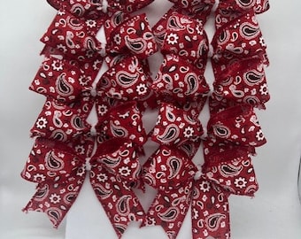 May include: A set of ten red and white bandana print bows. The bows are made of a soft, silky fabric and have a paisley pattern.