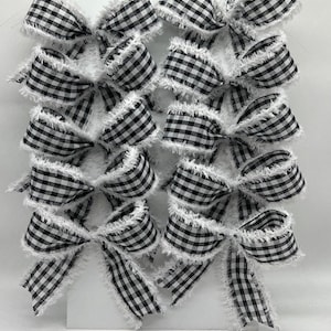 May include: A set of ten black and white gingham bows with frayed edges. The bows are tied with white ribbon and have a rustic farmhouse style.