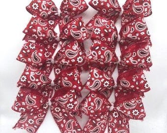 Pode incluir: Um conjunto de dezasseis laços de tecido vermelho dispostos numa grelha de quatro por quatro. Cada laço apresenta um padrão floral e paisley branco sobre um fundo vermelho, com bordas desfiadas e um nó central fixo.