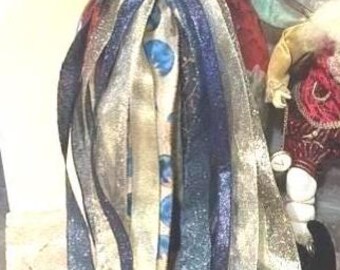 May include: A decorative hanging ornament featuring a large bow made of dark blue fabric with a silver branch pattern. Long, cascading ribbons in shades of navy blue, gold, and a light blue patterned print hang from the center button.