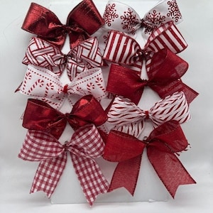 May include: A set of ten red and white Christmas bows. The bows are made of different materials, including plaid, striped, and solid red.