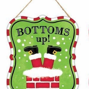 Può includere: Un cartello natalizio verde e rosso con bordo bianco e un gancio in corda bianca. Il cartello dice "Bottoms Up!" e presenta un Babbo Natale dei cartoni animati bloccato a testa in giù in un camino.