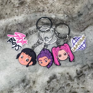 May include: Three keychains with cartoon character faces. Each keychain has a silver chain and ring. The faces are in black, purple, and pink, with the text "Pink Boys" and "Hunt X" on the tags.