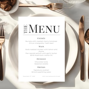 May include: A formal menu card with the title "THE MENU" in bold black letters. The menu lists Entrée, Main, Dessert, and Drinks. The menu is on a white plate with gold-colored silverware.