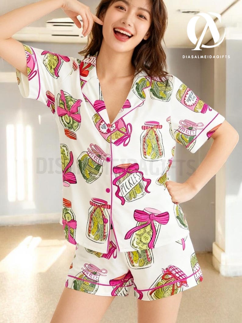A smiling woman wearing a white pajama top with a pattern of pickles and jars, posing in a room with a bright light source.