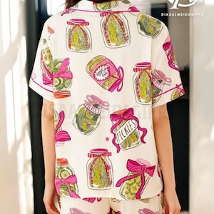 a person wearing a white shirt with a pattern of colorful illustrations of jars and pickles, along with pink bows.
